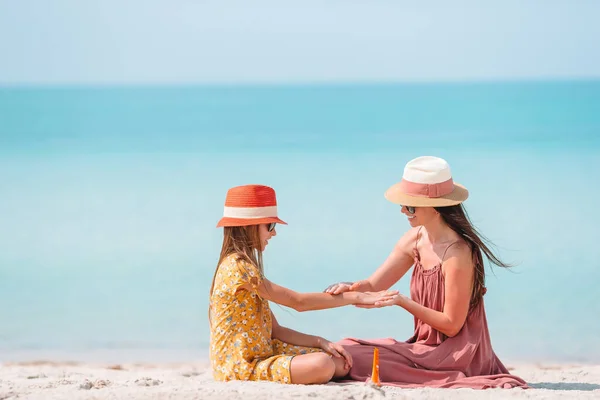 Jonge moeder brengt zonnecrème aan op dochter 's neus op het strand. Zonbescherming — Stockfoto