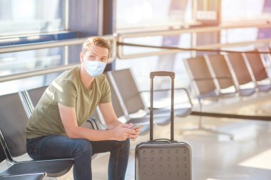 Havaalanı lobisindeki yolcu uçuş uçağını bekliyor. Havaalanında cep telefonu olan genç bir adam inişi bekliyor.