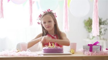 Beyaz kız rüyasında gülümsüyor ve gökkuşağı pastasına bakıyor. Balonlarla dolu renkli bir arka plan. Doğum günü partisi ve dilek konsepti.