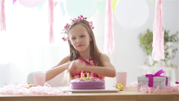 Chica caucásica está sonriendo de ensueño y mirando pastel de arco iris de cumpleaños. Fondo colorido festivo con globos. Fiesta de cumpleaños y el concepto de deseos . — Vídeo de stock