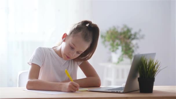 Ernste Schülerin sitzt mit Laptop und Schulbuch am Tisch und macht Hausaufgaben. — Stockvideo