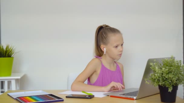 Écolière sérieuse assise à table avec ordinateur portable et manuel et faisant ses devoirs . — Video
