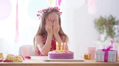 Beyaz kız rüyasında gülümsüyor ve gökkuşağı pastasına bakıyor. Balonlarla dolu renkli bir arka plan. Doğum günü partisi ve dilek konsepti.