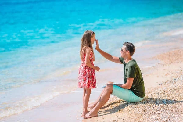 Padre aplicando crema de protección solar a su hija en la playa tropical — Foto de Stock