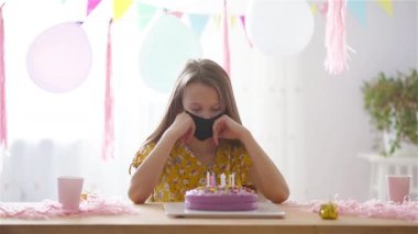 Beyaz kız doğum günü pastasına bakıyor. Balonlarla dolu renkli bir arka plan. Doğum günü partisi ve dilek konsepti.