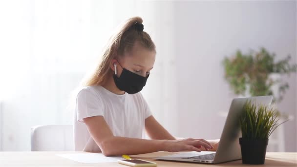 Seriös skolflicka sitter vid bordet med bärbar dator och lärobok och gör läxor. — Stockvideo