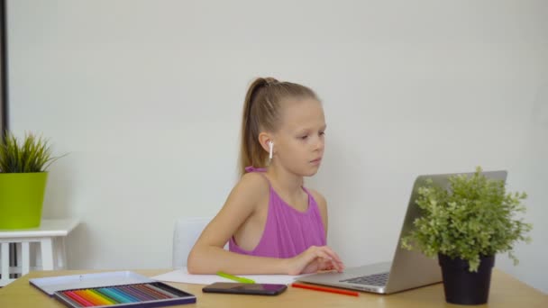 Serieuze schoolmeisje zitten aan tafel met laptop en leerboek en het doen van huiswerk. — Stockvideo