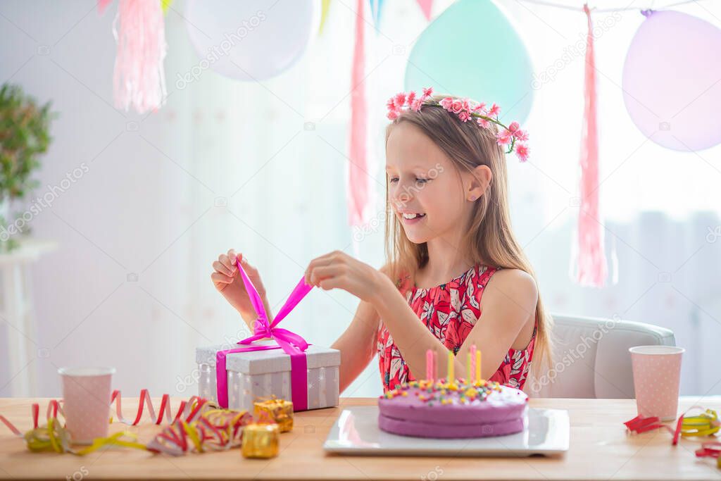 Caucasian girl is dreamily smiling and looking at birthday rainbow cake. Festive colorful background with balloons. Birthday party and wishes concept.