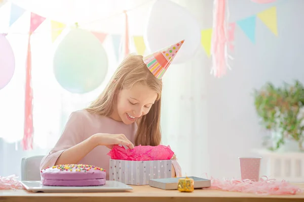 Blank meisje lacht dromerig en kijkt naar verjaardagsregenboogtaart. Feestelijke kleurrijke achtergrond met ballonnen. Verjaardagsfeest en wensenconcept. — Stockfoto