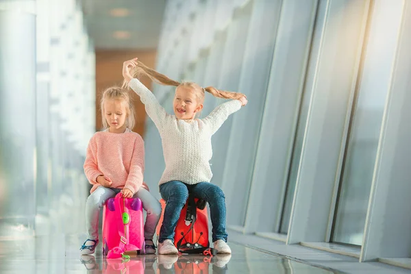 Adorables niñas divirtiéndose en el aeropuerto sentadas en la maleta esperando el embarque —  Fotos de Stock