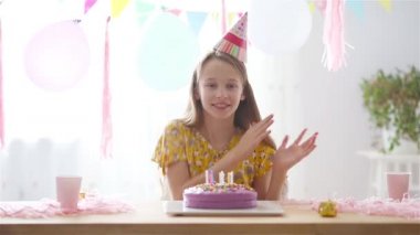 Beyaz kız rüyasında gülümsüyor ve gökkuşağı pastasına bakıyor. Balonlarla dolu renkli bir arka plan. Doğum günü partisi ve dilek konsepti.