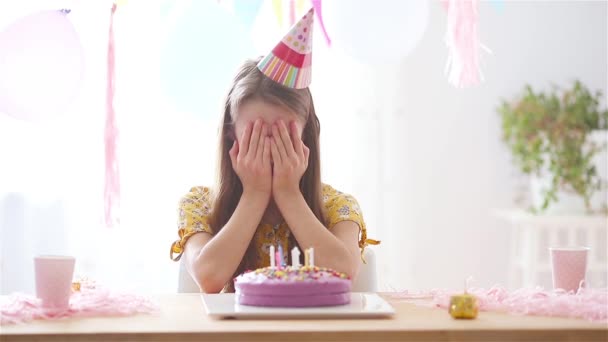 Blank meisje lacht dromerig en kijkt naar verjaardagsregenboogtaart. Feestelijke kleurrijke achtergrond met ballonnen. Verjaardagsfeest en wensenconcept. — Stockvideo