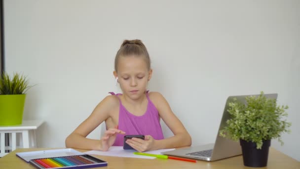 Colegiala seria sentada en la mesa con portátil y libro de texto y haciendo la tarea . — Vídeos de Stock