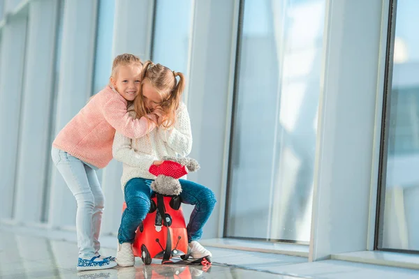 Adorable little girls having fun in airport sitting on suitcase waiting for boarding — Stock Photo, Image