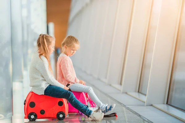 Adorables niñas divirtiéndose en el aeropuerto sentadas en la maleta esperando el embarque —  Fotos de Stock