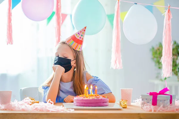 Caucasian girl is dreamily smiling and looking at birthday rainbow cake. Festive colorful background with balloons. Birthday party and wishes concept. — Stock Photo, Image