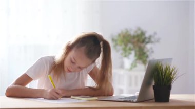 Ciddi liseli kız dizüstü bilgisayar ve ders kitabı ile masada oturuyor ve ödev yapıyor..