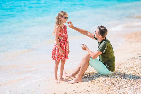Papá joven aplicando crema solar a la nariz de la hija en la playa. Protección solar —  Fotos de Stock