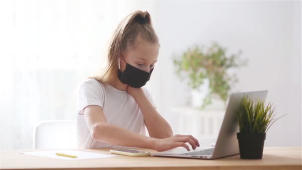 Colegiala seria sentada en la mesa con portátil y libro de texto y haciendo la tarea . — Vídeos de Stock