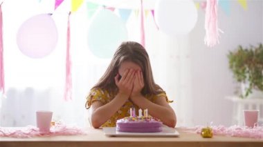 Beyaz kız doğum gününde maske takıyor. Balonlarla dolu renkli bir arka plan. Doğum günü partisi ve dilek konsepti.