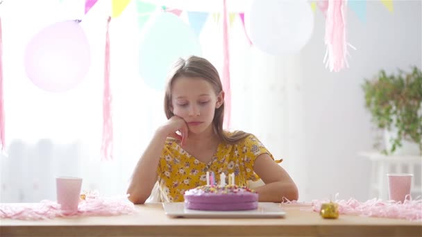 Caucasian girl is dreamily smiling and looking at birthday rainbow cake. Festive colorful background with balloons. Birthday party and wishes concept. — Stock Video