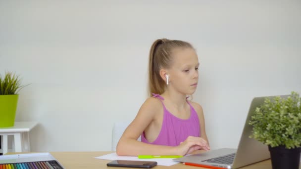 Colegiala seria sentada en la mesa con portátil y libro de texto y haciendo la tarea . — Vídeos de Stock