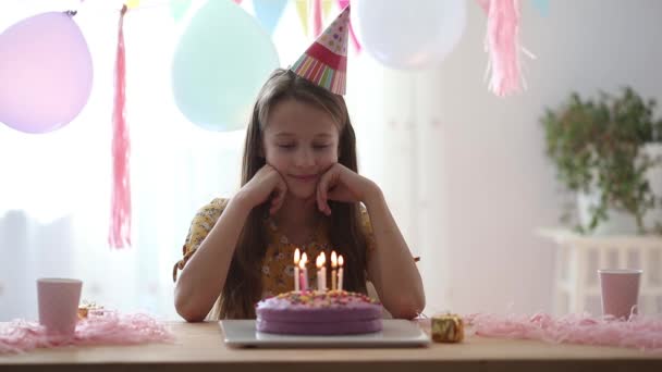 Blank meisje lacht dromerig en kijkt naar verjaardagsregenboogtaart. Feestelijke kleurrijke achtergrond met ballonnen. Verjaardagsfeest en wensenconcept. — Stockvideo