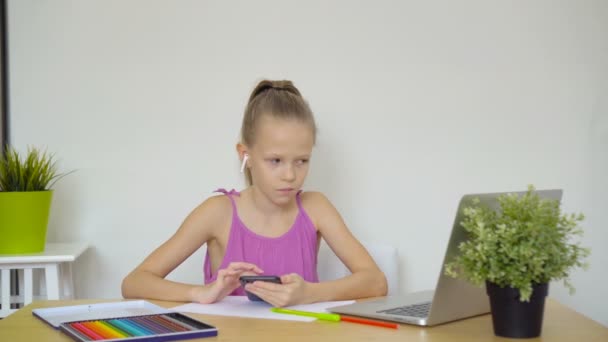 Komoly iskoláslány ül az asztalnál laptoppal, tankönyvvel és házi feladatot csinál..