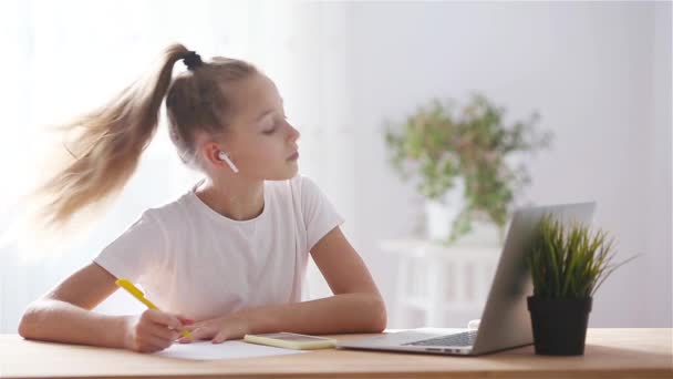 Serieuze schoolmeisje zitten aan tafel met laptop en leerboek en het doen van huiswerk. — Stockvideo