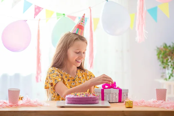 Blank meisje lacht dromerig en kijkt naar verjaardagsregenboogtaart. Feestelijke kleurrijke achtergrond met ballonnen. Verjaardagsfeest en wensenconcept. — Stockfoto