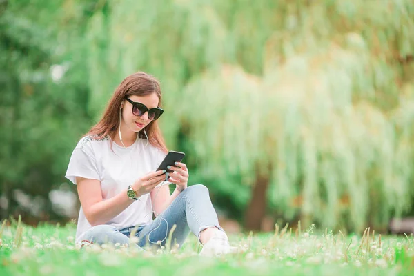 Roztomilá žena čte textovou zprávu na mobilním telefonu, zatímco sedí v parku. — Stock fotografie