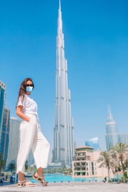 Maskeli mutlu kadın Dubai 'de arka planda gökdelenle yürüyor..