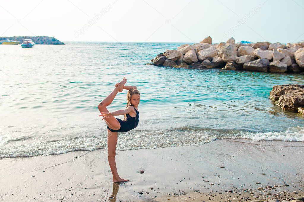 Active little girl at beach having a lot of fun. Cute kid making sporty exercises on the seashore