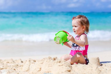 Tropik beyaz sahildeki küçük kız kumdan kale yapıyor.