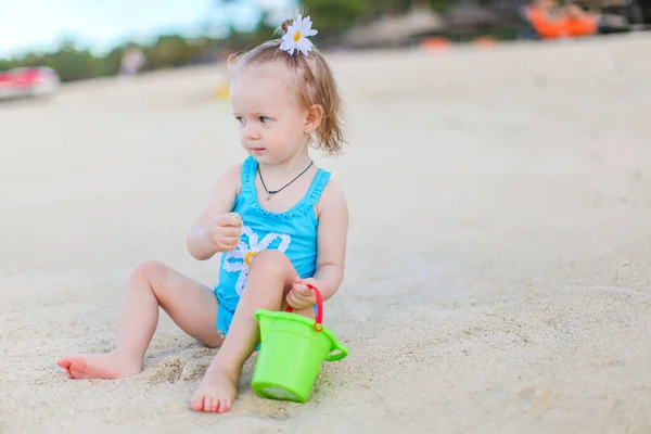 Маленькая девочка на тропическом белом пляже строит замок из песка — стоковое фото