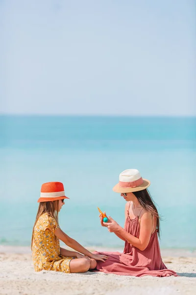 Jonge moeder brengt zonnecrème aan op dochter 's neus op het strand. Zonbescherming — Stockfoto