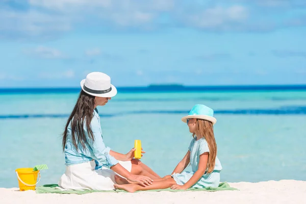 Jonge moeder brengt zonnecrème aan op dochter 's neus op het strand. Zonbescherming — Stockfoto