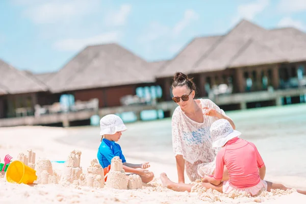 Mãe e filhas fazendo castelo de areia na praia tropical — Fotografia de Stock