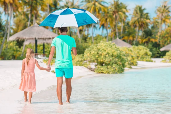 Junger Vater und seine kleine Tochter spazieren unter Sonnenschirm am weißen Sandstrand — Stockfoto