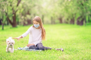 Parkta virüsü önlemek için köpekli küçük bir kız koruyucu maske takıyor.