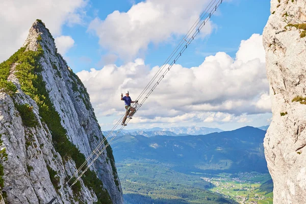 Yaz aylarında ferrata ile Donnerkogel 'i ara, çapraz merdivene tırmanırken zafer işareti gösteren bir adamla. Cennete giden merdiven kavramı.