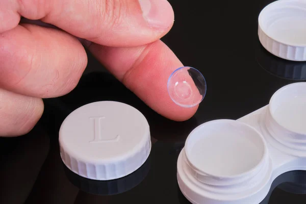 Beyaz lens kutusu ve kapağı olan parmak ucunda torik kontak lens - siyah yansıtıcı arka planda bileşim.