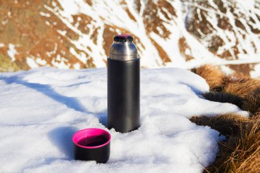 Kış yürüyüşlerinde sıcak içecek olarak kullanılan yeniden kullanılabilir vakum şişesi, Romanya 'nın Fagaras dağlarında (Karpatlar' ın bir kısmı) yanında bir fincan çayla kara yatırıldı.