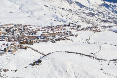 La Toussuire dağ köyü Les Sybelles kayak sahasında dağın tepesinden görülmektedir. Güneşli bir günde kış manzarası.