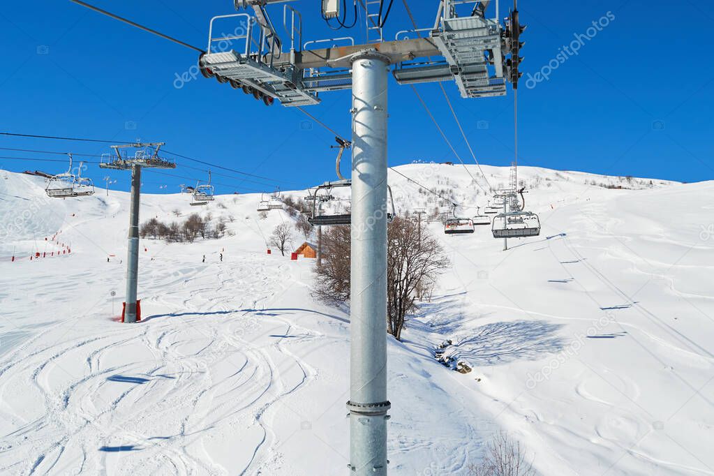 View from a moving ski chair lift in Winter, high above the ground, in Les Sybelles ski domain, France, on a day with perfect blue skies. S-line curve shapes in off piste terrain, below the chairlift.