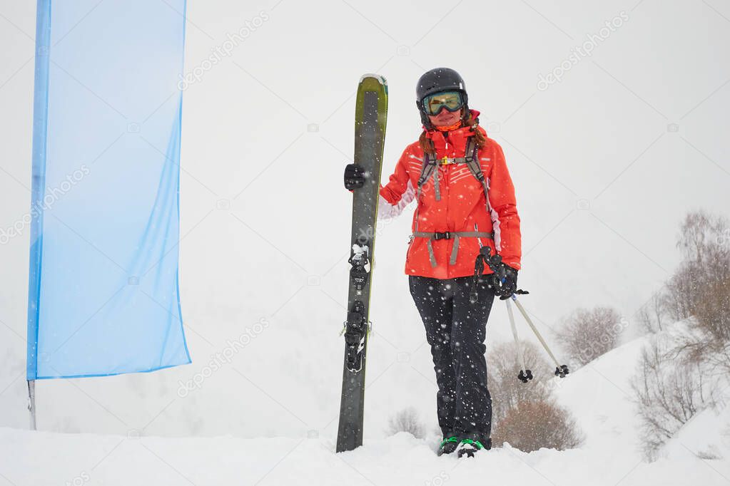 Freerider woman skier with fat/wide all mountain skis posing next to a blank blue flag, during a whiteout day in Les Sybelles ski resort, France.