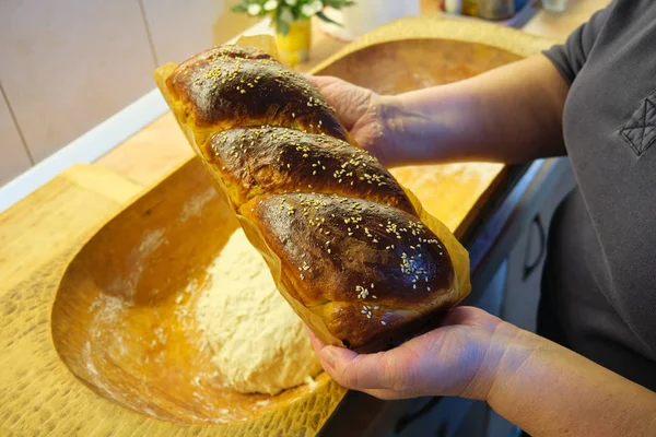 Traditional Romanian and Bulgarian baked pastry called Cozonac/Kozunak held by a woman cook in her hands, above a wooden trough with dough in it. Home made sweet dessert - over the shoulder view.