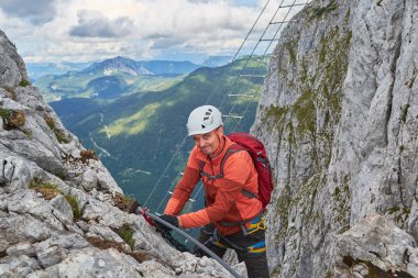 Ferrata Intersport, Donnerkogel Dağı, Avusturya üzerinden halat değiştirirken kameraya doğru göz kırpan tırmanıcı.