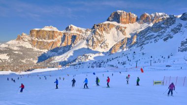 Sabahın erken saatlerinde, Dolomiti Superski bölgesinde Sellaronda pistinde gün doğumunda yanan Sella grubuyla birlikte yamaçlarda kayakçılar..