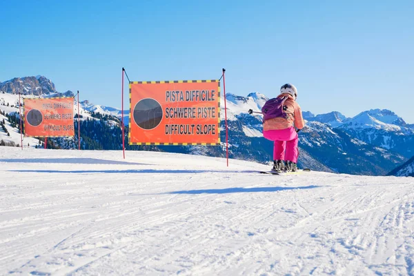 Woman skier starting a black ski run, reserved for experts only, passing two warning signs saying Difficult Slope in Italian, German, and English, during the Sellaronda ski tour in Dolomites, Italy.